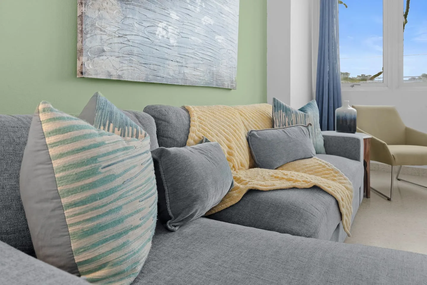 Grey couch with a yellow throw blanket on it — Maré 2BR | Near Ocean Park Beach + Laundry, Santurce