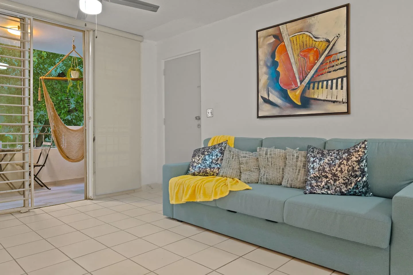 Blue couch with yellow pillows and a painting above it — San Juan 2BR | Sleeps 7 + Balcony & Laundry, Santurce