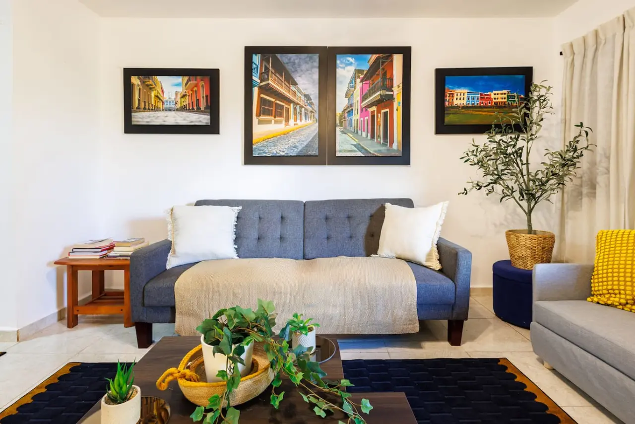 Living room with a gray sofa under three street paintings — Ocean Sol Historic Old San Juan