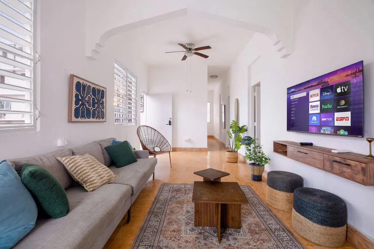 Living room with a gray sofa, a TV and a long hallway — Luz Collection No.3 – Casa Horizonte | 3BR Loft, Santurce