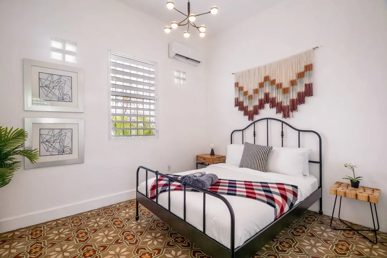 Bedroom with a black iron bed and a woven wall hanging — Luz Collection No.2 – Casa Brisa | 3BR Retreat, Santurce