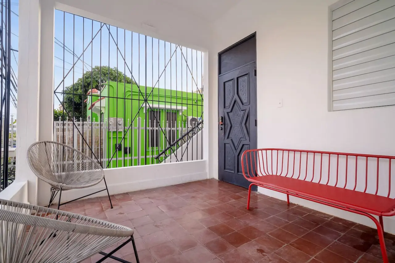Covered front veranda with a red bench and chairs — Luz Collection No.2 – Casa Brisa | 3BR Retreat, Santurce