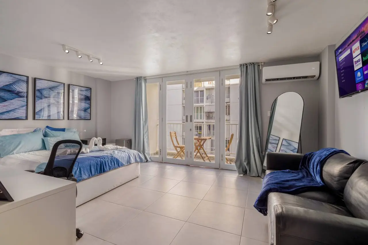 Living area with a bed, a leather sofa and balcony doors — OceanSide - Pool Balcony, Isla Verde