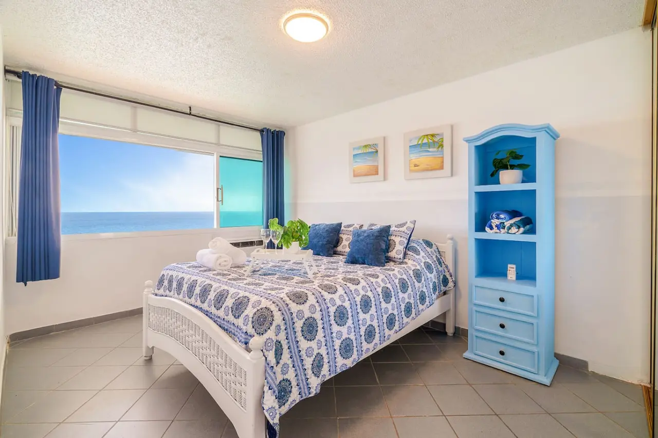 Bedroom with a blue bedspread and white headboard — Captain’s Beachfront Luquillo Beach House