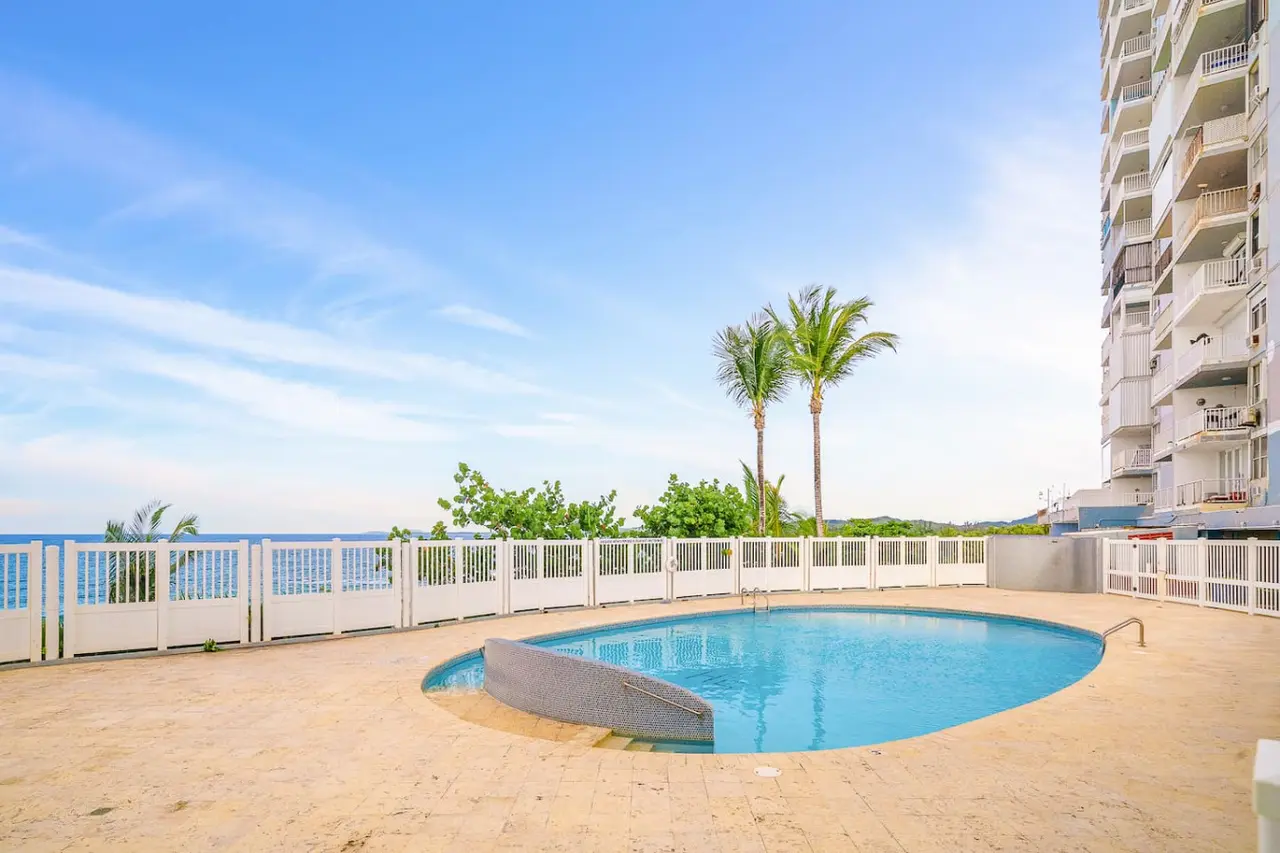 Fenced pool by the sea with palm trees — Captain’s Beachfront Luquillo Beach House