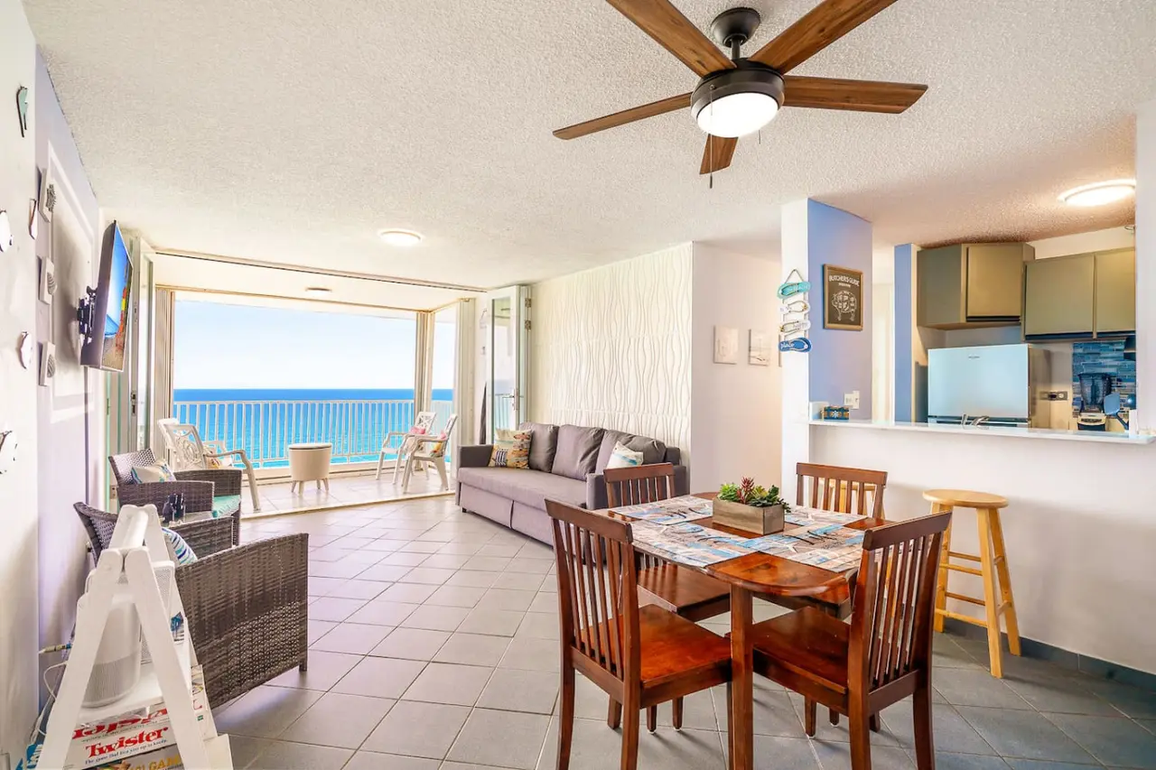 Living area with a dining table, open kitchen and balcony — Captain’s Beachfront Luquillo Beach House