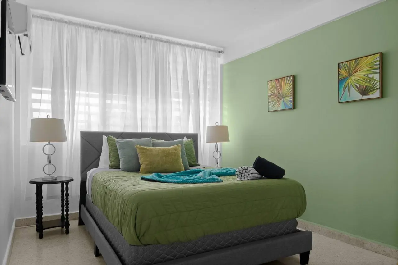 Bedroom with a large bed, a lamp, and a green wall — Maré 2BR | Near Ocean Park Beach + Laundry, Santurce