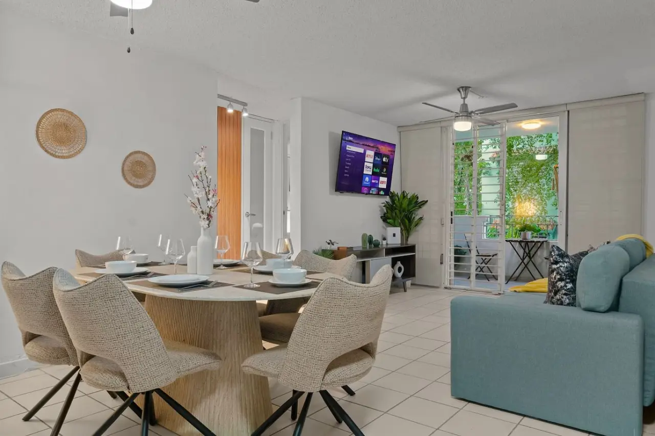 Dining room table with chairs and a TV in the background — San Juan 2BR | Sleeps 7 + Balcony & Laundry, Santurce