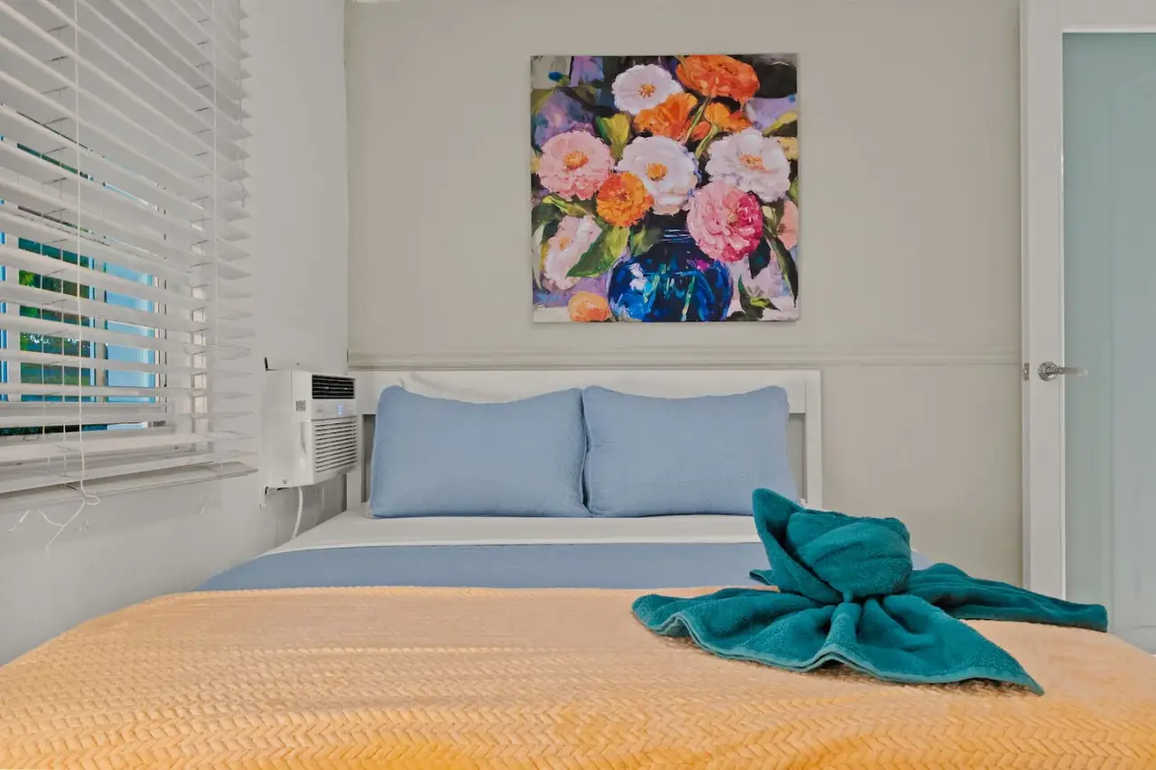 Bedroom with a blue bedspread and a painting of flowers on the wall — San Juan 2BR | Sleeps 7 + Balcony & Laundry, Santurce