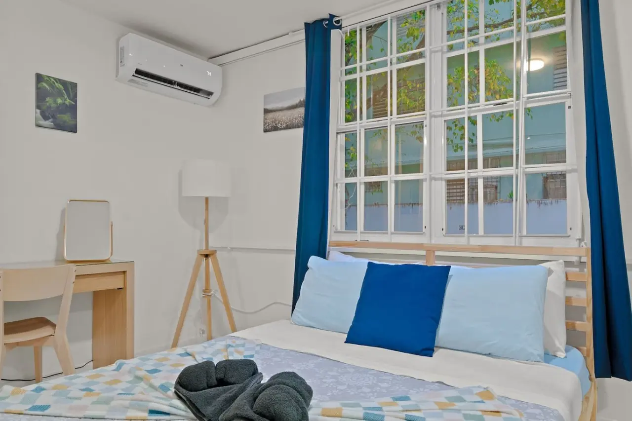 Bedroom with a blue bedspread and a view of the window — The Castillo | Sleeps 8 | 2BR + Backyard & Parking, Santurce