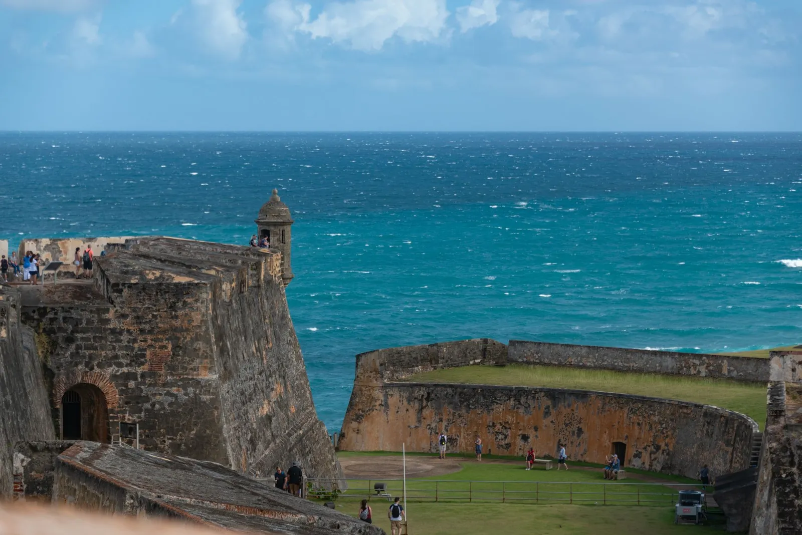 A view of the historic El Morro Fort in Puerto Rico with a backdrop of the ocean and people exploring.