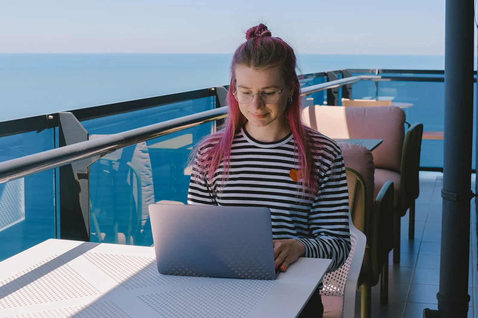 A laptop open on a sunny oceanfront balcony.